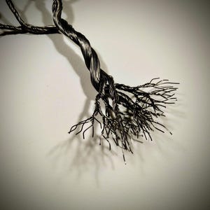 May include: A metal sculpture of a tree with a twisted trunk and many branches. The sculpture is made of thin wire and has a dark, metallic finish.