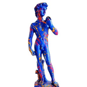 Könnte beinhalten: Blaue David-Statue mit roten und gelben Farbspritzern. Die Skulptur steht auf einem rechteckigen Sockel. Die Statue ist ein dekorativer Gegenstand.