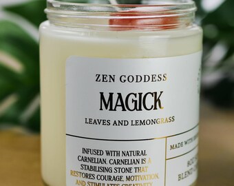 Puede incluir: Un tarro de vela blanco con una etiqueta dorada que dice "ZEN GODDESS MAGICK LEAVES AND LEMONGRASS". La etiqueta también dice "INFUSED WITH NATURAL CARNELIAN. CARNELIAN IS A STABILISING STONE THAT RESTORES COURAGE, MOTIVATION, AND STIMULATES CREATIVITY." El tarro de vela tiene un cristal rojo en la parte superior.