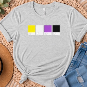 May include: A light heather grey short-sleeved t-shirt featuring a graphic print of four rectangular colour swatches in yellow, white, purple, and black. Each swatch is labelled with its corresponding colour name in black text below the block.