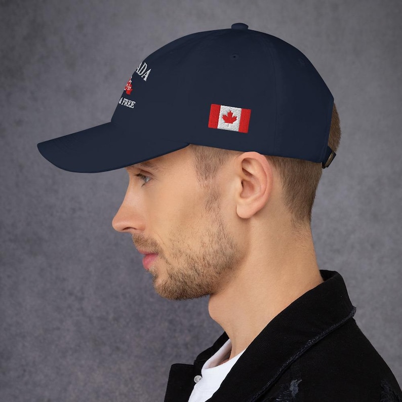 May include: A navy blue baseball cap with the text "CANADA" and "IS FREE" embroidered on the front. The Canadian flag is embroidered on the right side of the cap.