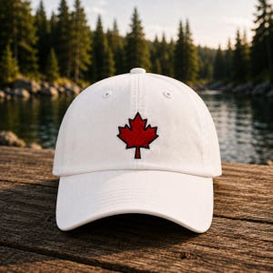May include: A white baseball cap featuring a central, embroidered red maple leaf design. The cap has a structured crown, a curved brim, and stitched eyelets on the top panels. The design is clean, simple, and focuses on the iconic leaf symbol.