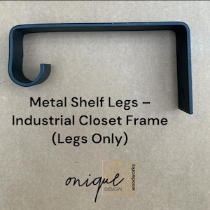 May include: A matte black metal shelf bracket featuring a flat horizontal arm and a curved hook end, with a vertical mounting plate containing two circular screw holes. The text Metal Shelf Legs – Industrial Closet Frame (Legs Only) is visible.
