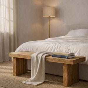 以下が含まれることがあります： 明るい色のスローがかけられた素朴な木製のベンチ。2冊の本と水を入れたグラスがベンチの上に置かれています。ベージュのシェードのフロアランプと白いリネンのベッドが背景にあります。ベンチの長さは約120cmです。