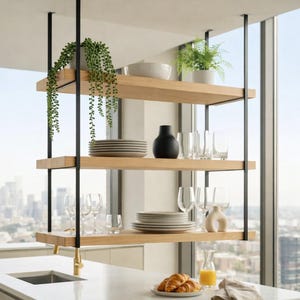 May include: A three-tiered, hanging kitchen shelf with black metal supports and light wood shelves. The shelves display plates, glasses, a black vase, and potted plants. A cityscape is visible through the window.