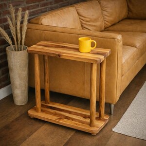 May include: A rectangular wooden side table with a smooth top surface, four cylindrical legs, and a matching bottom shelf. The table is crafted from light brown wood with visible grain patterns and sits on a flat floor surface.