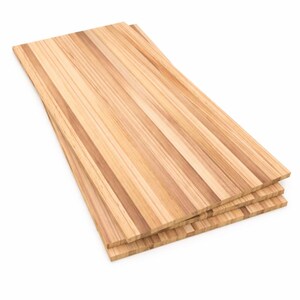 May include: A stack of three rectangular wooden boards featuring a natural light brown grain pattern with alternating darker vertical stripes. The boards are layered on top of each other, showcasing a smooth, flat surface and clean, straight edges.