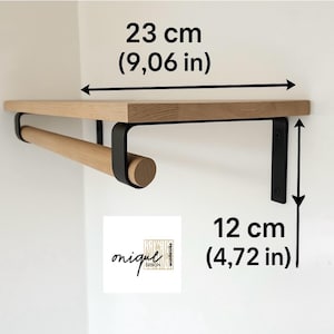 May include: A wall-mounted wooden shelf with a light wood grain finish and a matching wooden rod underneath, supported by two black metal brackets. The shelf measures 23 cm in width and 12 cm in height. A logo reads onique design.