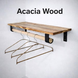 May include: Wooden shelf made from acacia wood, featuring a wooden rod and black metal brackets. The shelf has a natural wood grain finish. Three metal hangers hang from the rod. The text "Acacia Wood" is above the shelf.