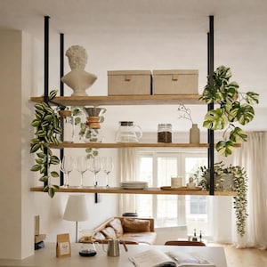 Könnte beinhalten: Ein dreistufiges, abgehängtes Holzregal mit schwarzen Metallstützen. Die Regale zeigen dekorative Gegenstände wie eine Büste, Kisten, Glaswaren, Kaffeezubereitungsgeräte und Pflanzen. Die Einheit befindet sich in einer hellen, modernen Küche.