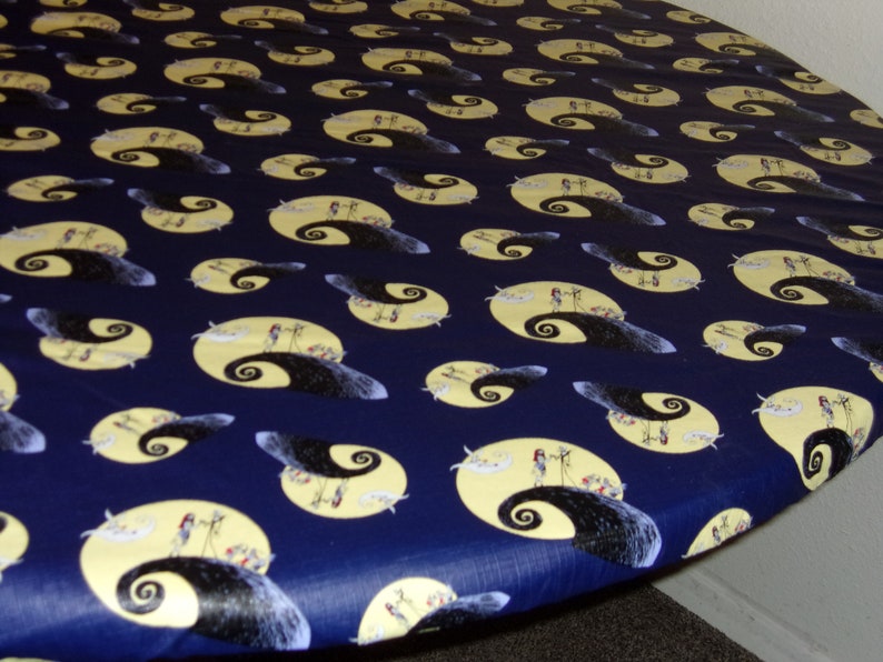 Peut inclure: Une nappe ronde bleue avec un motif r&eacute;p&eacute;t&eacute; d'une lune jaune et une silhouette noire d'une colline avec un chemin sinueux. La colline est tir&eacute;e du film L'&Eacute;trange No&euml;l de monsieur Jack.