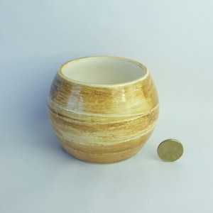 May include: A small, round, ceramic planter with a brown and white striped glaze. The planter is sitting on a white surface.