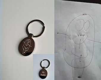 May include: Silver keychain with a round oval charm. The charm has a child's drawing of a person with a smiling face engraved on it. The text "My Daddy" is engraved on the back of the charm.