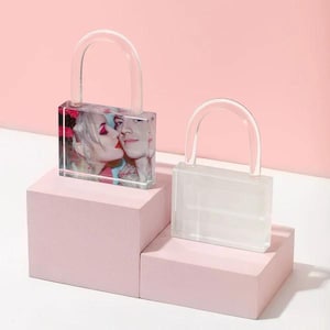 Könnte beinhalten: Zwei transparente Acryl-Bilderrahmen in Form eines Schlosses mit einem Foto eines Paares in einem Rahmen und einem leeren Platz im anderen Rahmen. Die Rahmen stehen auf rosa Plattformen.
