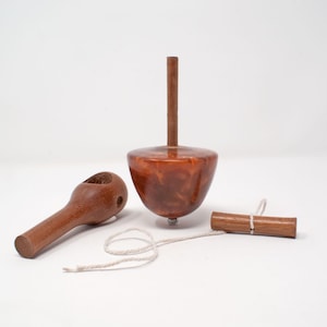 Peut inclure: Un ensemble de toupie en bois avec une finition marron. L'ensemble comprend le dessus, une poignée et une ficelle. Le dessus mesure environ 10 cm de haut. La poignée sert à lancer le dessus.