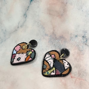 May include: Heart-shaped earrings with a patchwork design. The earrings feature a variety of colours, including pink, brown, and blue, and are outlined with a black border. Each earring has a black stud and gold-coloured loop.