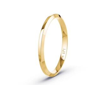 May include: A polished yellow gold ring with a faceted, angular band design. The metal surface reflects light, highlighting the sharp edges and smooth finish of the circular jewelry piece. The interior of the band features small engraved text.