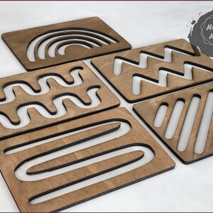 May include: Five wooden tracing boards with different geometric patterns cut out. The patterns include a rainbow, zigzags, wavy lines, stripes, and curved lines.