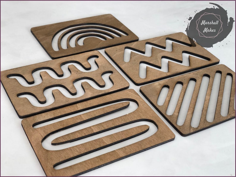 May include: Five wooden tracing boards with different geometric patterns cut out. The patterns include a rainbow, zigzags, wavy lines, stripes, and curved lines.