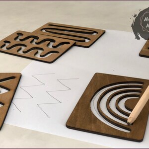 May include: Wooden stencils with various geometric patterns, including waves, zigzags, stripes, and a rainbow. The stencils are on a white surface with a pencil tracing the outline of the rainbow stencil.