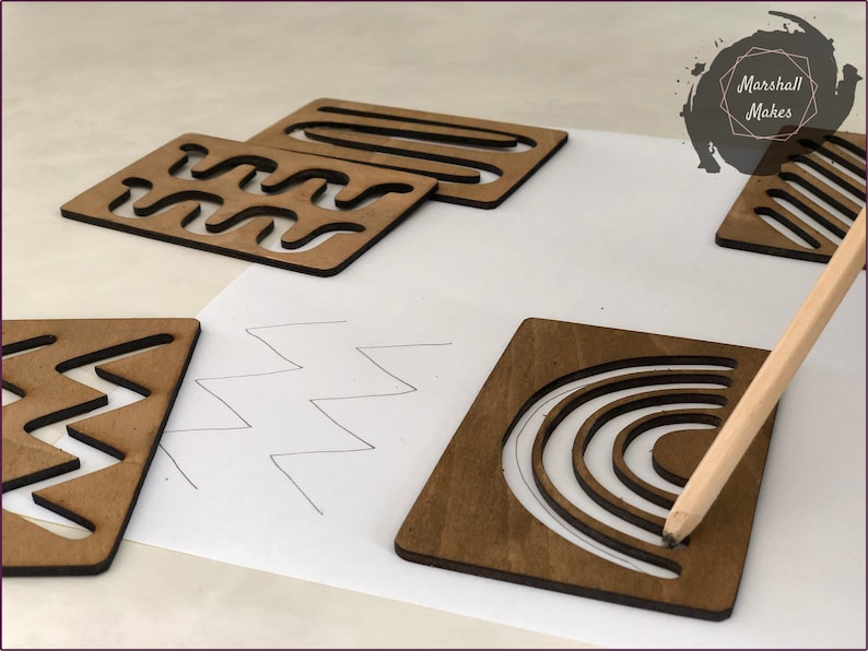 May include: Wooden stencils with various geometric patterns, including waves, zigzags, stripes, and a rainbow. The stencils are on a white surface with a pencil tracing the outline of the rainbow stencil.