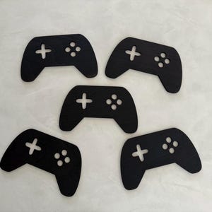 May include: Five black wooden game controller cutouts. The controllers are all the same size and shape, and they have the standard buttons and directional pad.