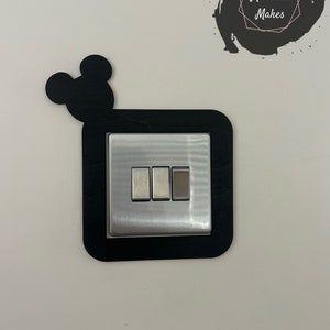 May include: Black wooden light switch cover with Mickey Mouse ears. The switch cover has three buttons.