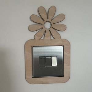 May include: A light switch with a wooden frame and a daisy design. The switch has three buttons.