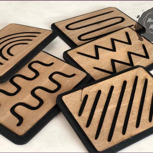 May include: Six wooden tiles with black borders and different line patterns. The patterns include a rainbow, wavy lines, zigzags, straight lines, and a curved shape. The tiles are arranged in a pile.