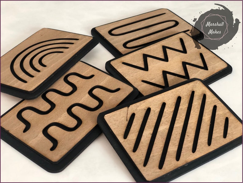 May include: Six wooden tiles with black borders and different line patterns. The patterns include a rainbow, wavy lines, zigzags, straight lines, and a curved shape. The tiles are arranged in a pile.