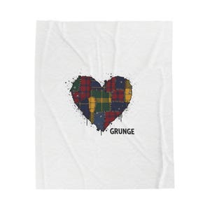 Può includere: Coperta bianca con un design a forma di cuore realizzato in tessuto patchwork a quadri rossi, blu, gialli e verdi. La parola "GRUNGE" è stampata in nero sotto il cuore, con schizzi di vernice nera intorno.