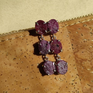 Può includere: Un paio di orecchini pendenti con tre pietre di rubino viola su ogni orecchino. Le pietre sono incastonate in argento.