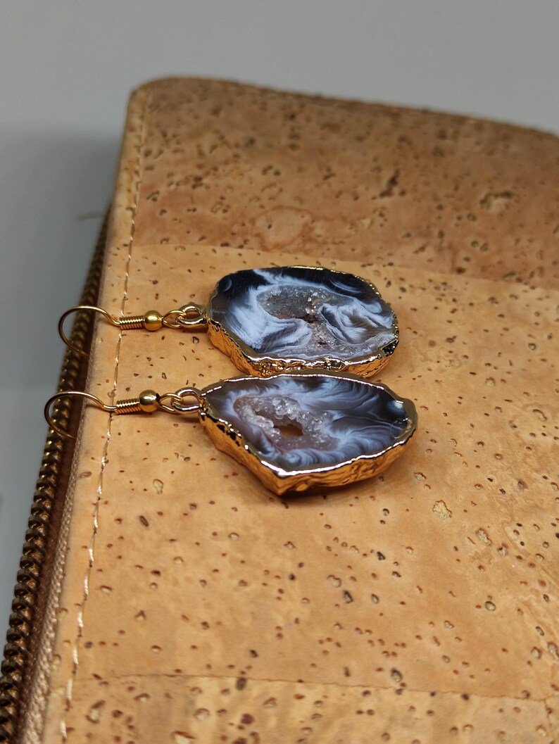 Puede incluir: Un par de pendientes de tono dorado con una piedra de &aacute;gata blanca y gris. Las piedras tienen una forma irregular y un aspecto natural y org&aacute;nico.
