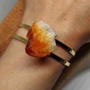 May include: A gold double-band bracelet with a large, raw, orange and white citrine crystal attached.
