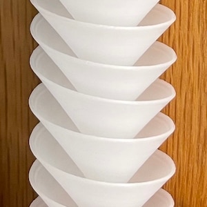 May include: A stack of white ceramic funnels, nested together, with a wooden background.