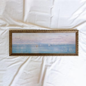 May include: A panoramic landscape painting in a decorative gold-toned frame featuring a calm blue sea with several small sailboats under a soft, pale sky with light clouds. The artwork depicts a serene maritime scene with a wide horizontal orientation.