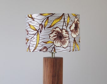 May include: A table lamp with a wooden base and a white lampshade with a floral pattern in yellow, brown, and white.
