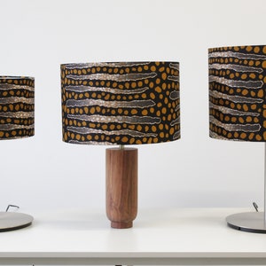 May include: Three table lamps with different sized bases and shades. The shades are all black with a brown and white geometric pattern. The bases are silver metal, wood, and silver metal.