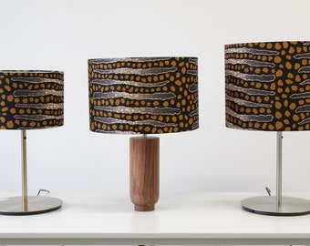 May include: Three table lamps with different sized bases and shades. The shades are all black with a brown and white geometric pattern. The bases are silver metal, wood, and silver metal.