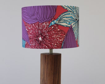 May include: A wooden table lamp with a cylindrical base and a colorful floral patterned lampshade. The lampshade features pink, purple, and blue flowers on a red background.