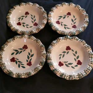 May include: Set of four white ceramic pie plates with green and red floral designs. Each plate has a scalloped edge.