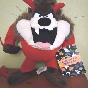 May include: A red and brown plush bean bag toy of Taz the Tasmanian Devil dressed as a devil for Halloween. The toy has a tag that reads "Devilish Taz Bean Bag".