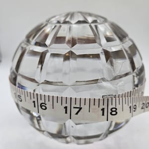 May include: Clear, faceted glass sphere with a tape measure wrapped around it. The sphere appears to be approximately 17 inches in diameter. The glass has a geometric pattern and is transparent.