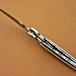 May include: A closed pocket knife with a patterned blade and a bone handle. The knife has a brass pin and a brass bolster.