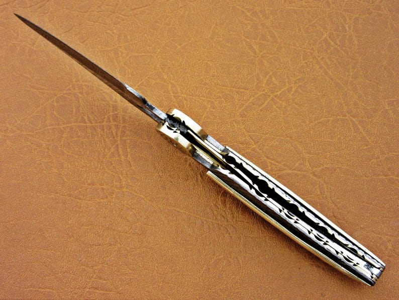 May include: A closed pocket knife with a patterned blade and a bone handle. The knife has a brass pin and a brass bolster.