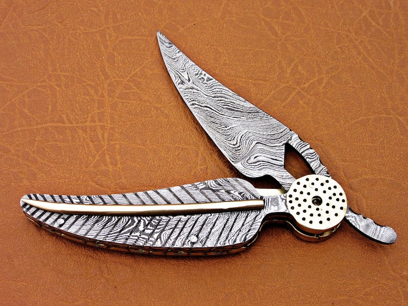 May include: A silver pocket knife with a patterned blade and a brass handle. The blade is open and the handle is shaped like a feather.