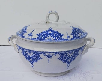 Puede incluir: Un plato de servir de cerámica blanca con un patrón floral azul y blanco. El plato tiene una tapa con un asa de anillo y dos asas laterales.