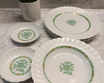 May include: Set of four white ceramic plates with a green and gold floral design. The plates have a scalloped edge and are stacked on top of each other.