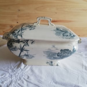 Op de afbeelding: Een witte porseleinen serveerschaal met een blauw en wit bloemenpatroon. De schaal heeft een deksel met een handvat en is versierd met een landschapssc&egrave;ne.