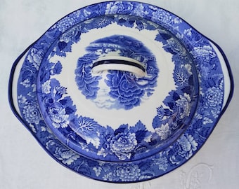 Puede incluir: Un plato de servir de porcelana azul y blanco con un patrón floral y una tapa. La tapa tiene una escena de paisaje azul y blanco con una pequeña casa y árboles.